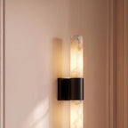Clérachic wall sconce with a black band and glowing alabaster column on a blush panelled wall, its shadow cast beside it.