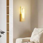 Lit Clérachic alabaster wall light with a gold-toned plate on a beige wall, beside a tall open shelf and the arm of a cream sofa.