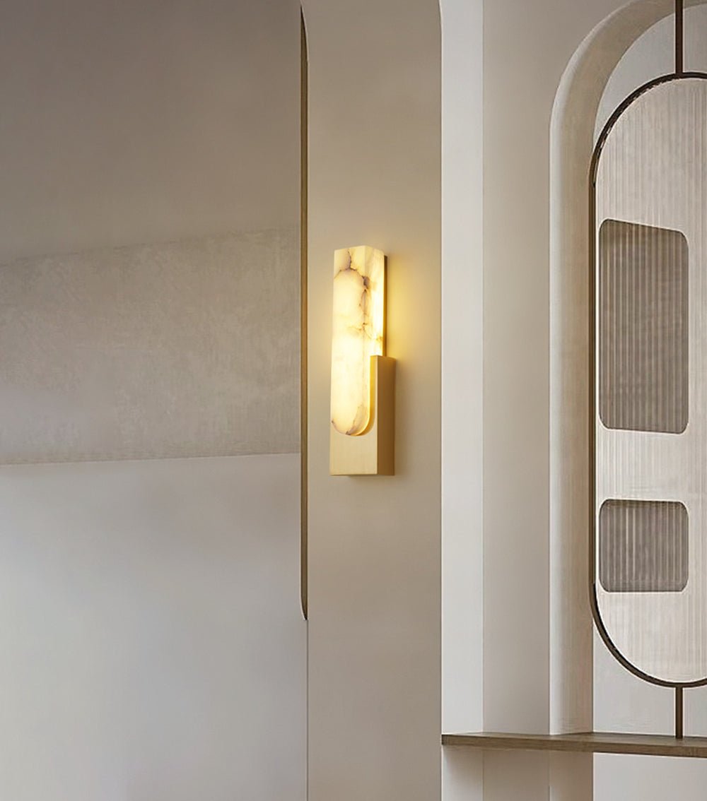 Second view of the gold-toned Clérachic wall light by the arched partition, with the alabaster bar glowing and the shelf ledge below.