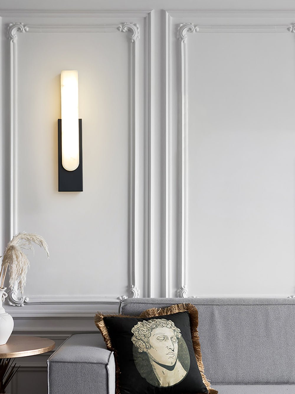 Black-backed Clérachic wall light lit on a white panelled wall above a grey sofa with a portrait cushion.