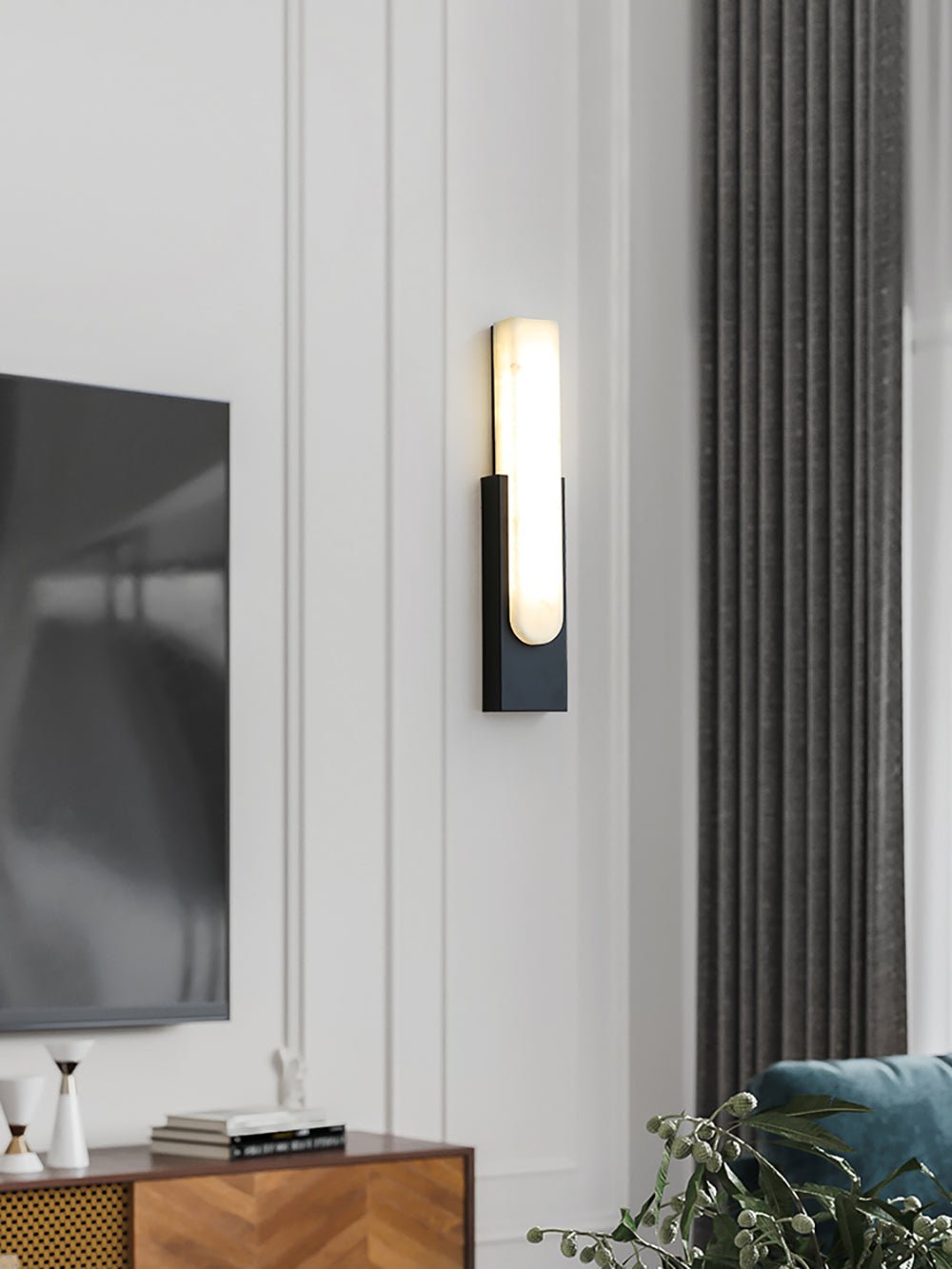 A Clérachic wall light with a black plate lit on a panelled wall, beside a television, grey curtains and a wood sideboard.