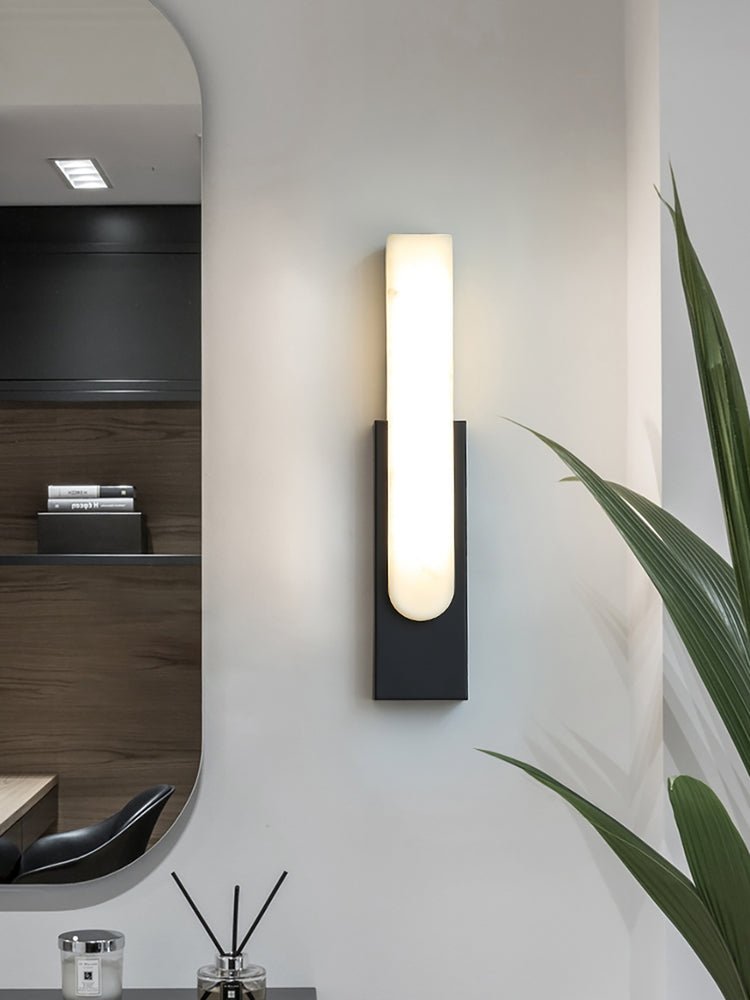 Black-backed Clérachic wall light, lit, in a hallway with an oval mirror, a reed diffuser and a spiky green plant.