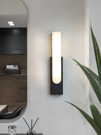 Black-backed Clérachic wall light, lit, in a hallway with an oval mirror, a reed diffuser and a spiky green plant.