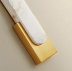 Close view of the polished gold back plate cradling the rounded end of the alabaster bar on this Clérachic wall light.