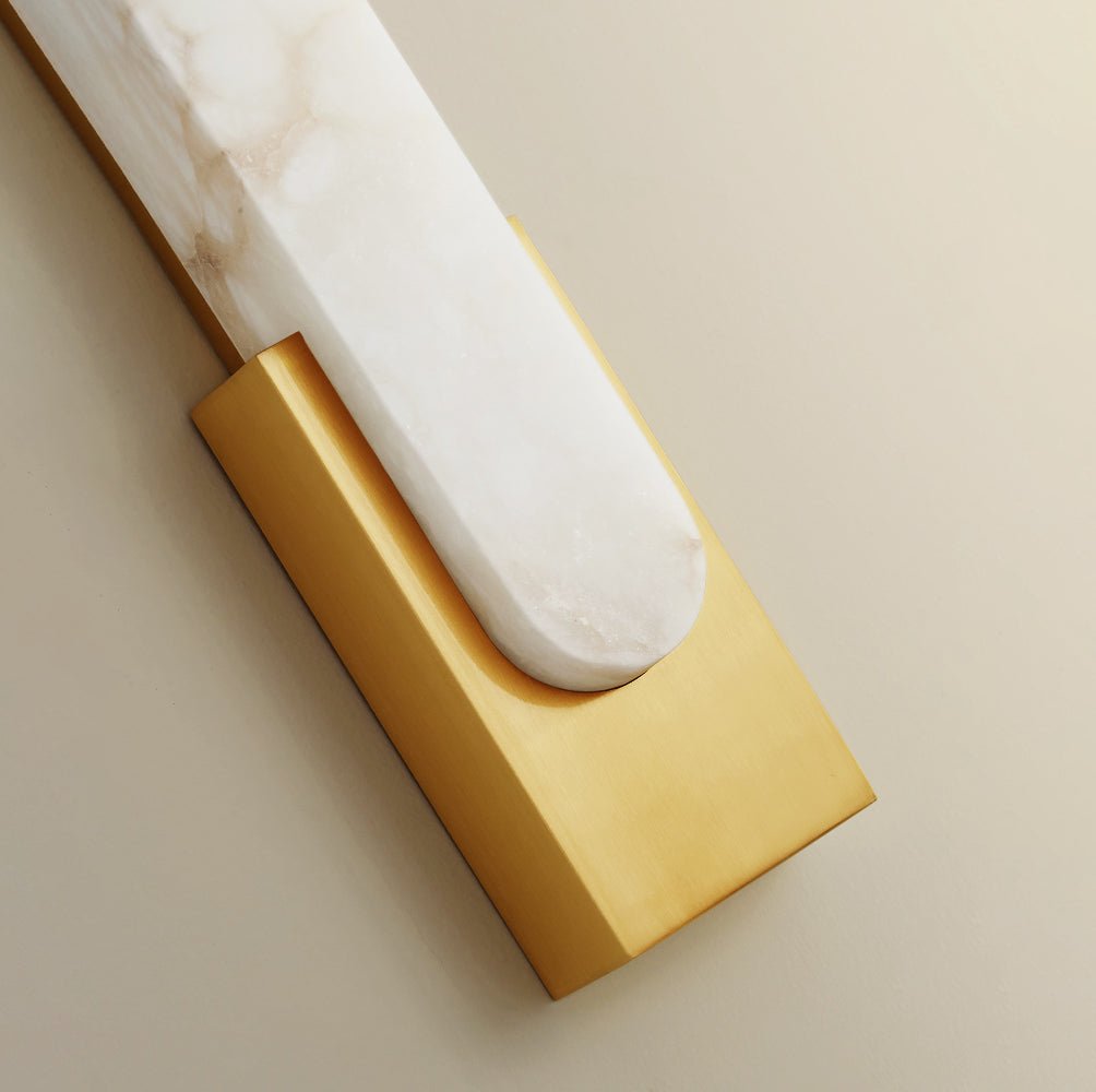Close view of the polished gold back plate cradling the rounded end of the alabaster bar on this Clérachic wall light.