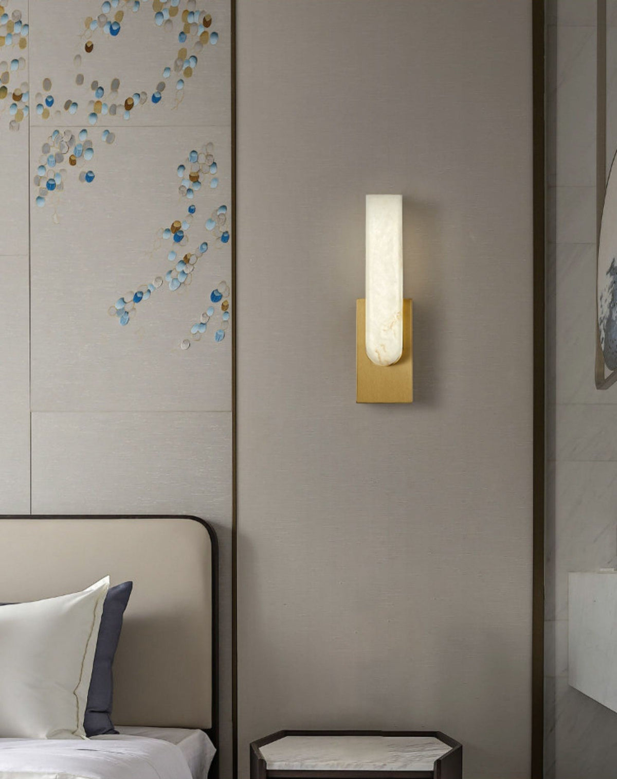 Gold-toned Clérachic wall light lit above a bedside table, on a panelled wall with a decorative blue and gold pattern.