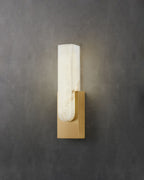 Gold-toned Clérachic wall light on a dark grey concrete-look wall, its pale alabaster bar lit softly from within.