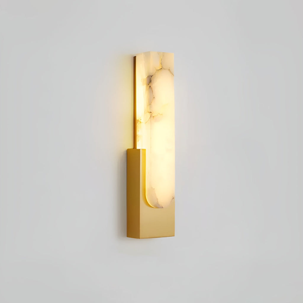 Lit gold-toned Clérachic wall light on a pale grey wall, with strong brown veining running through the alabaster bar.