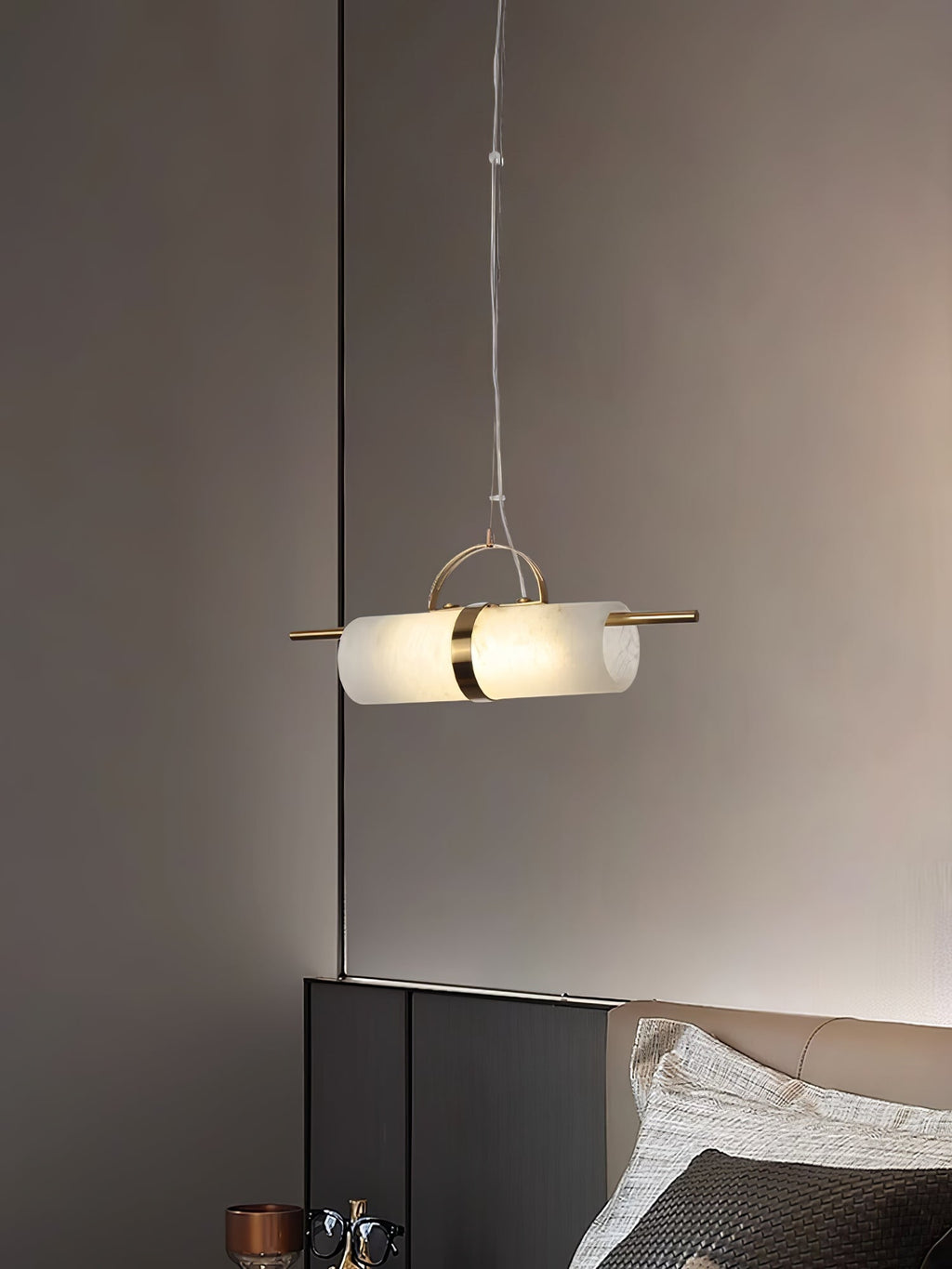 Clérachic Alabaster Cylinder LED Pendant Light hung as a bedside light beside a headboard, warm stone glowing against a taupe wall.