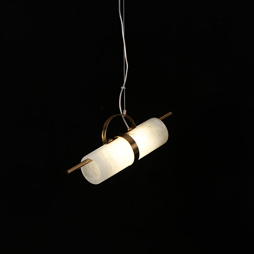 Clérachic Alabaster Cylinder LED Pendant Light lit against black, the stone tube tilted on its copper rod and half-loop hanger.