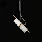 Clérachic Alabaster Cylinder LED Pendant Light switched off against black, showing the raw white stone with its copper band and rod.