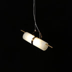 Clérachic Alabaster Cylinder LED Pendant Light angled on its cable against black, the copper band catching light at the tube's centre.