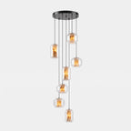 A cluster of seven clear glass Clérachic pendants hangs at staggered heights from a round black canopy on a pale grey backdrop.