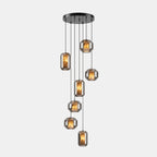 A cluster of seven smoke grey glass Clérachic pendants hangs at staggered heights from a round black canopy on a pale backdrop.