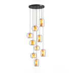A larger cluster of clear glass Clérachic pendants with amber-lit alabaster hangs at staggered heights from a round black canopy on white.