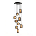 A larger cluster of smoke grey glass Clérachic pendants with amber-lit alabaster hangs at staggered heights from a round black canopy on white.