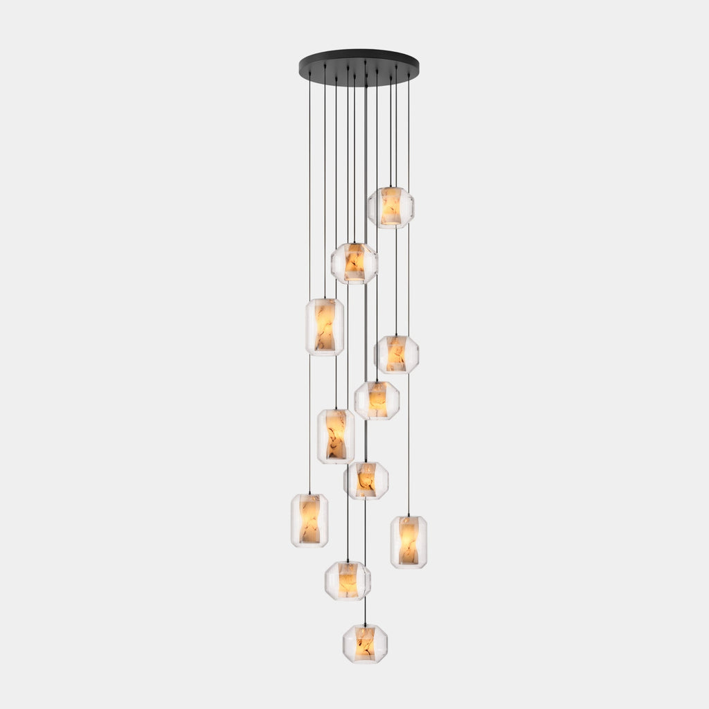 A long cluster of clear glass Clérachic pendants hangs at many heights from a wide round black canopy on a pale grey backdrop.