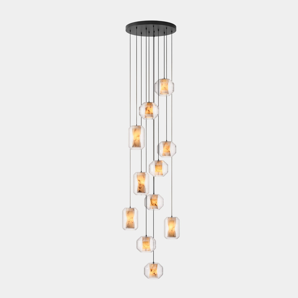 A long cluster of clear glass Clérachic pendants hangs at many heights from a wide round black canopy on a pale grey backdrop.