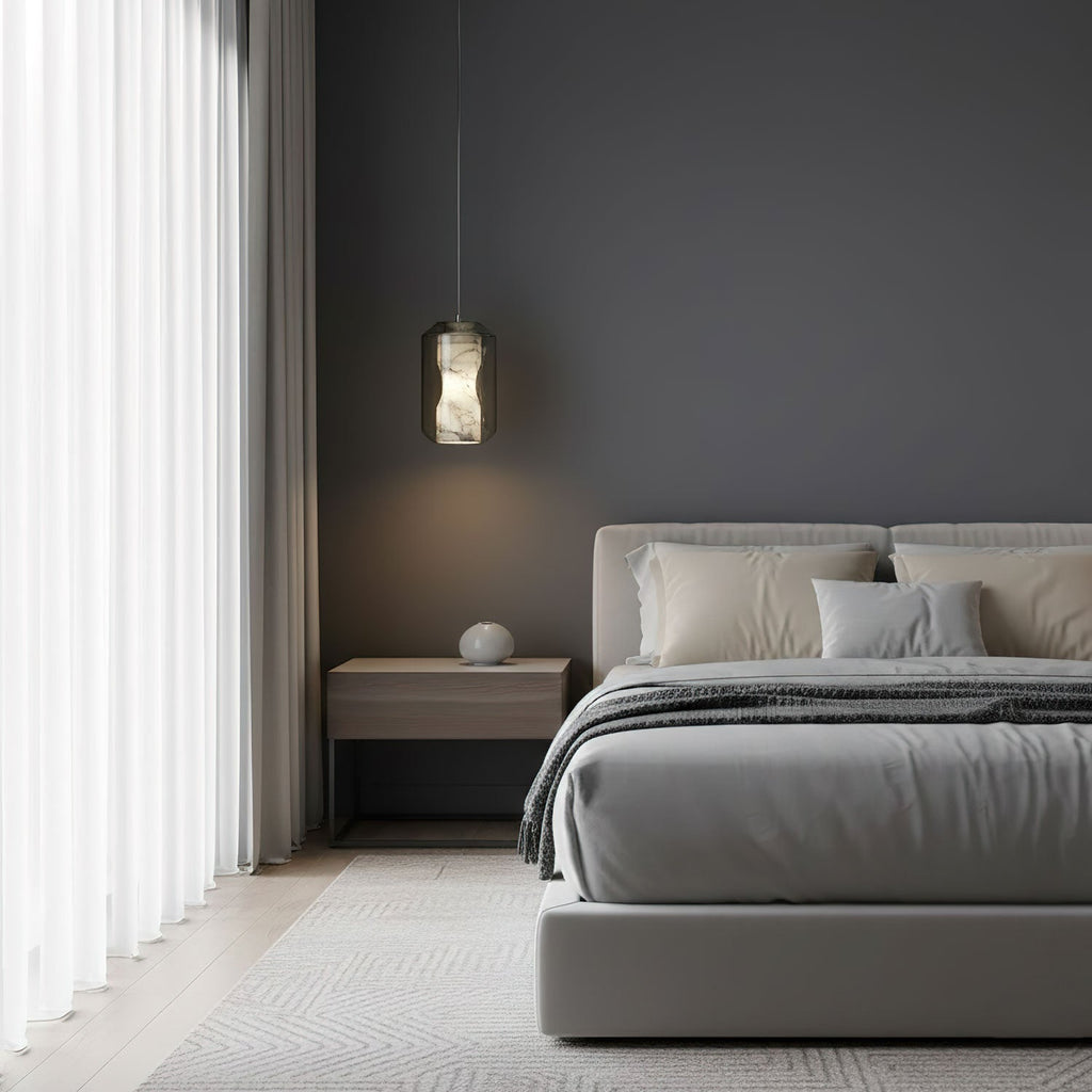 A single Clérachic alabaster pendant on a thin cord hangs against a dark grey bedroom wall, above a low bed with pale linen.