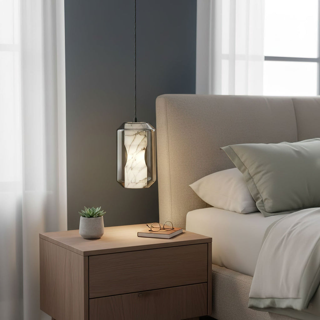 This Clérachic pendant hangs beside a light wooden bedside table with a small plant, its alabaster core glowing against a dark grey wall.