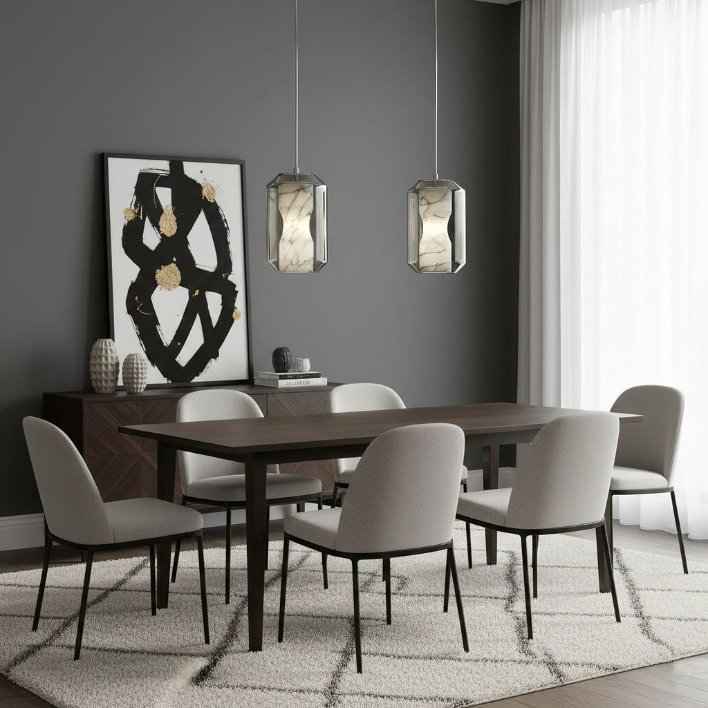 Two Clérachic alabaster pendants hang side by side over a dark wood dining table with grey chairs, in front of a black and gold artwork.