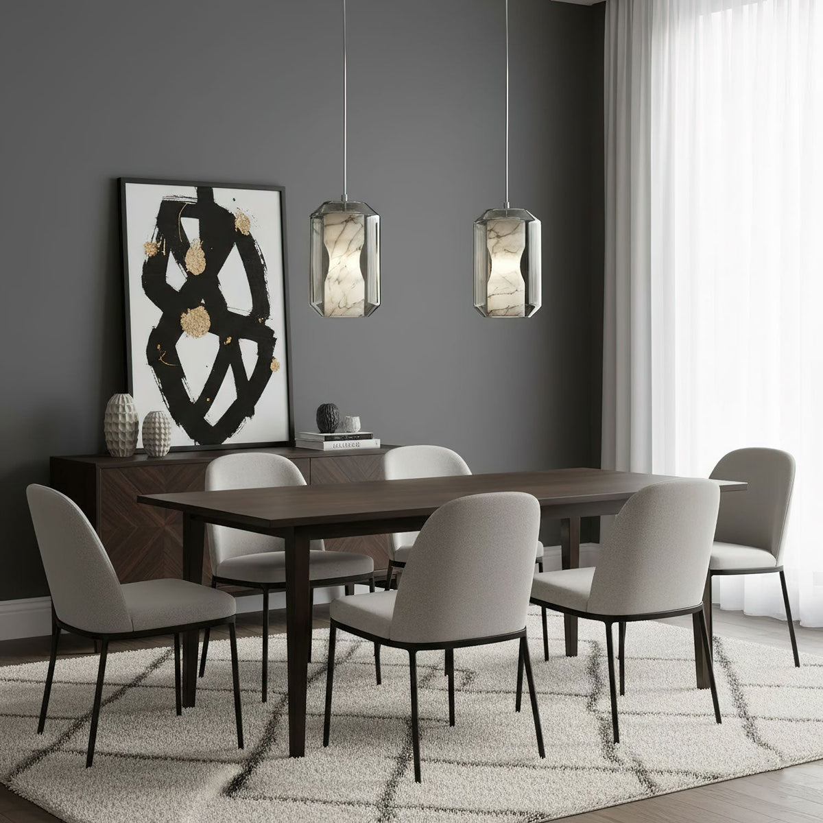 Two Clérachic alabaster pendants hang side by side over a dark wood dining table with grey chairs, in front of a black and gold artwork.