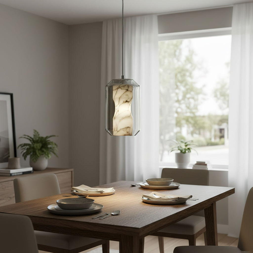 One Clérachic alabaster pendant lit warm above a walnut dining table set for a meal, with a window and a small plant behind.