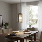 One Clérachic alabaster pendant lit warm above a walnut dining table set for a meal, with a window and a small plant behind.