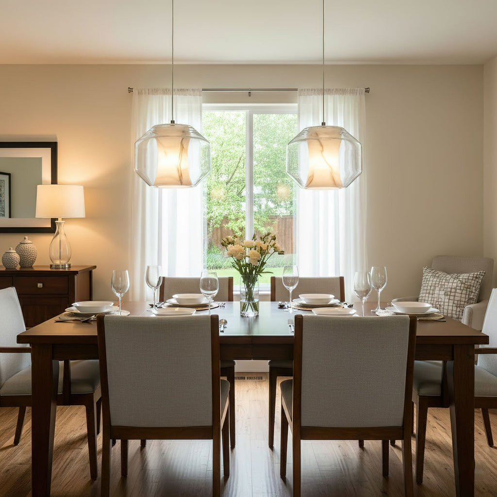 Two clear-shelled Clérachic pendants glow amber over a laid dining table in a cream room, with sheer curtains and a garden window behind.