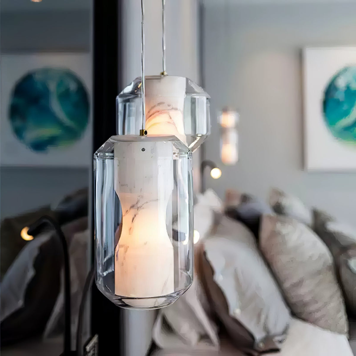 Close, softly focused view of two of these Clérachic pendants, the white-veined alabaster glowing inside clear glass above a cushioned bed.