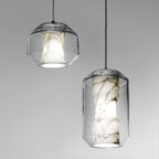 Two Clérachic pendants on a plain grey backdrop, a short wide one and a tall one, each with white alabaster veined in brown inside clear glass.
