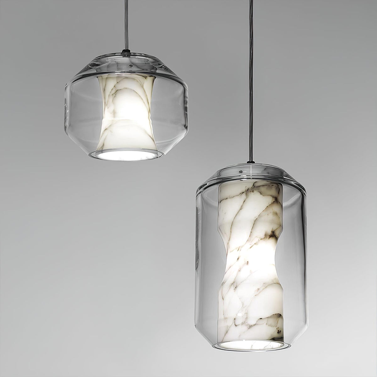 Two Clérachic pendants on a plain grey backdrop, a short wide one and a tall one, each with white alabaster veined in brown inside clear glass.