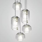 Five Clérachic pendants at staggered heights on a pale grey backdrop, cylinder and rounded-faceted glass shells each holding a veined alabaster core.