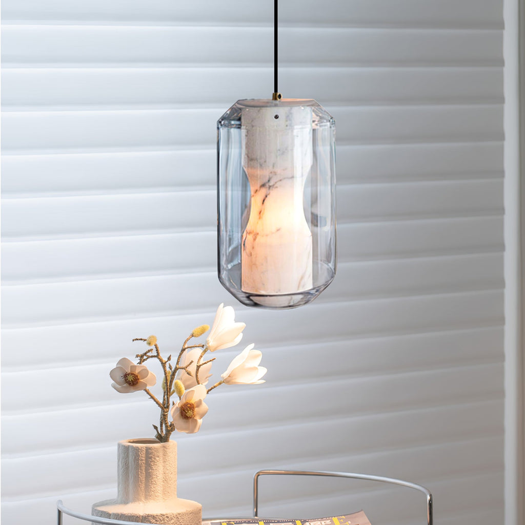 Clérachic alabaster pendant glowing warm in front of white slatted blinds, with a pale ceramic vase of magnolia blossom below.