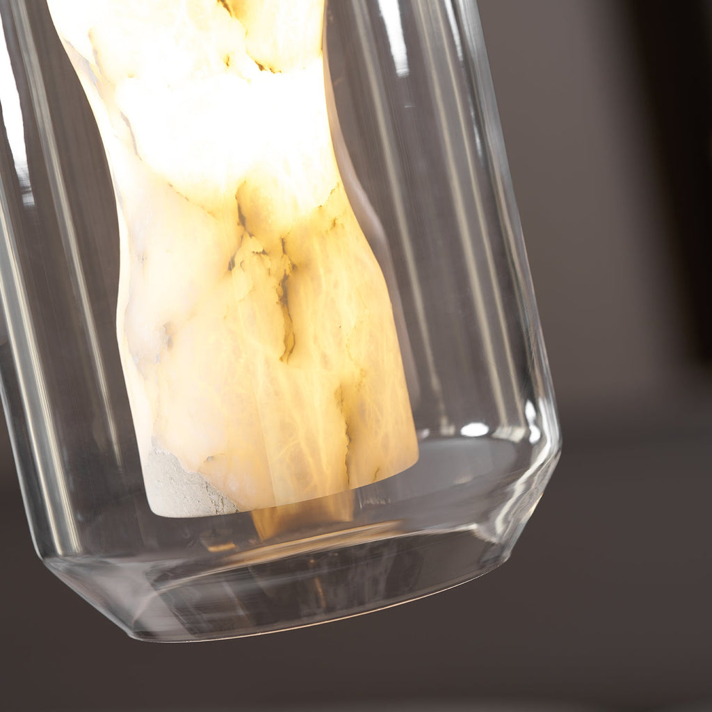 Close view of the lit alabaster column and the clear glass rim at the base of this Clérachic pendant, against a dark blurred background.