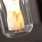 Close view of the lit alabaster column and the clear glass rim at the base of this Clérachic pendant, against a dark blurred background.