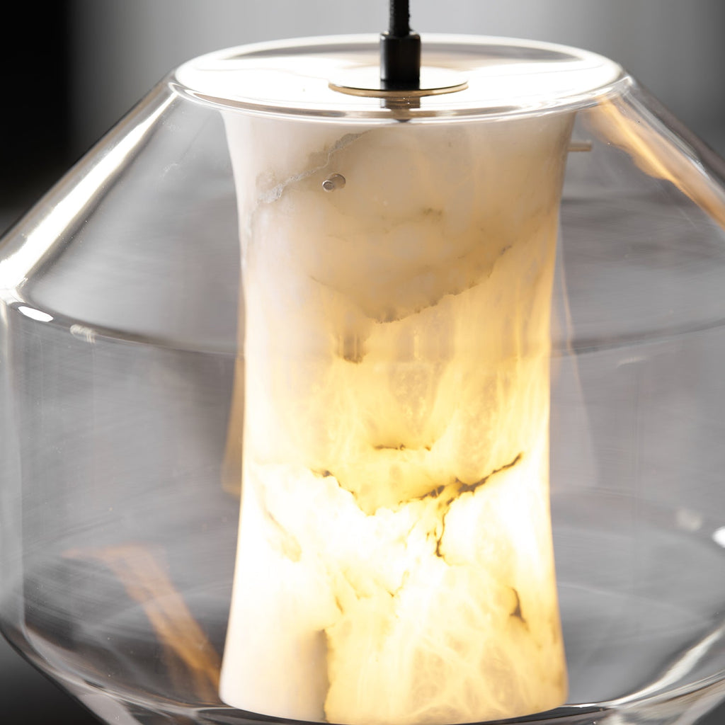 Very close view of the brass-toned ring and black cord at the top of this Clérachic pendant, with the alabaster glowing warm inside a wide glass shell.