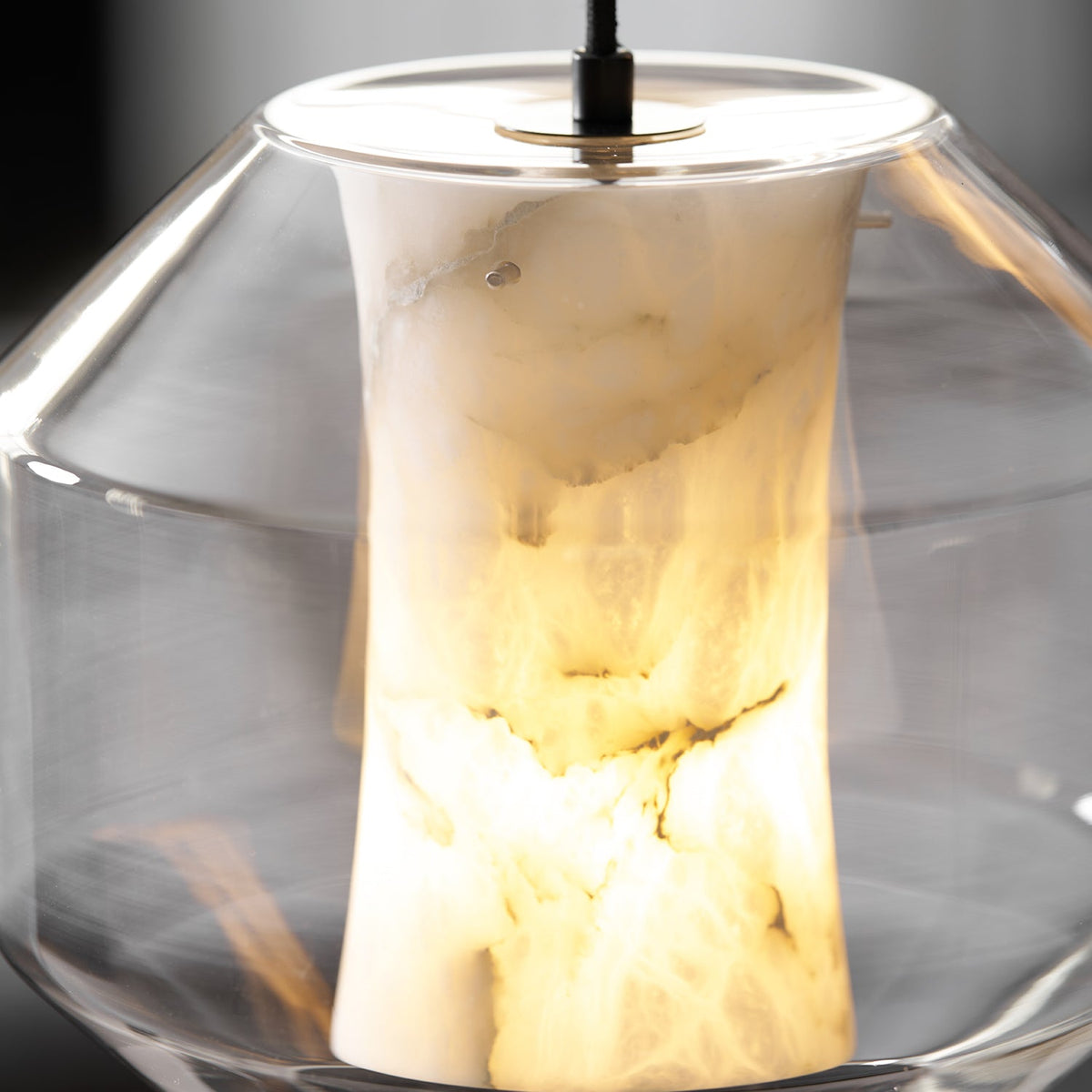 Close view of the warm-lit alabaster column, its cloudy white and amber veining clear inside the wide glass shell of this Clérachic pendant.
