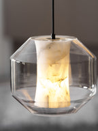 A wide, faceted-glass Clérachic pendant on a black cord, its white alabaster column lit warm against a blurred dark wall.