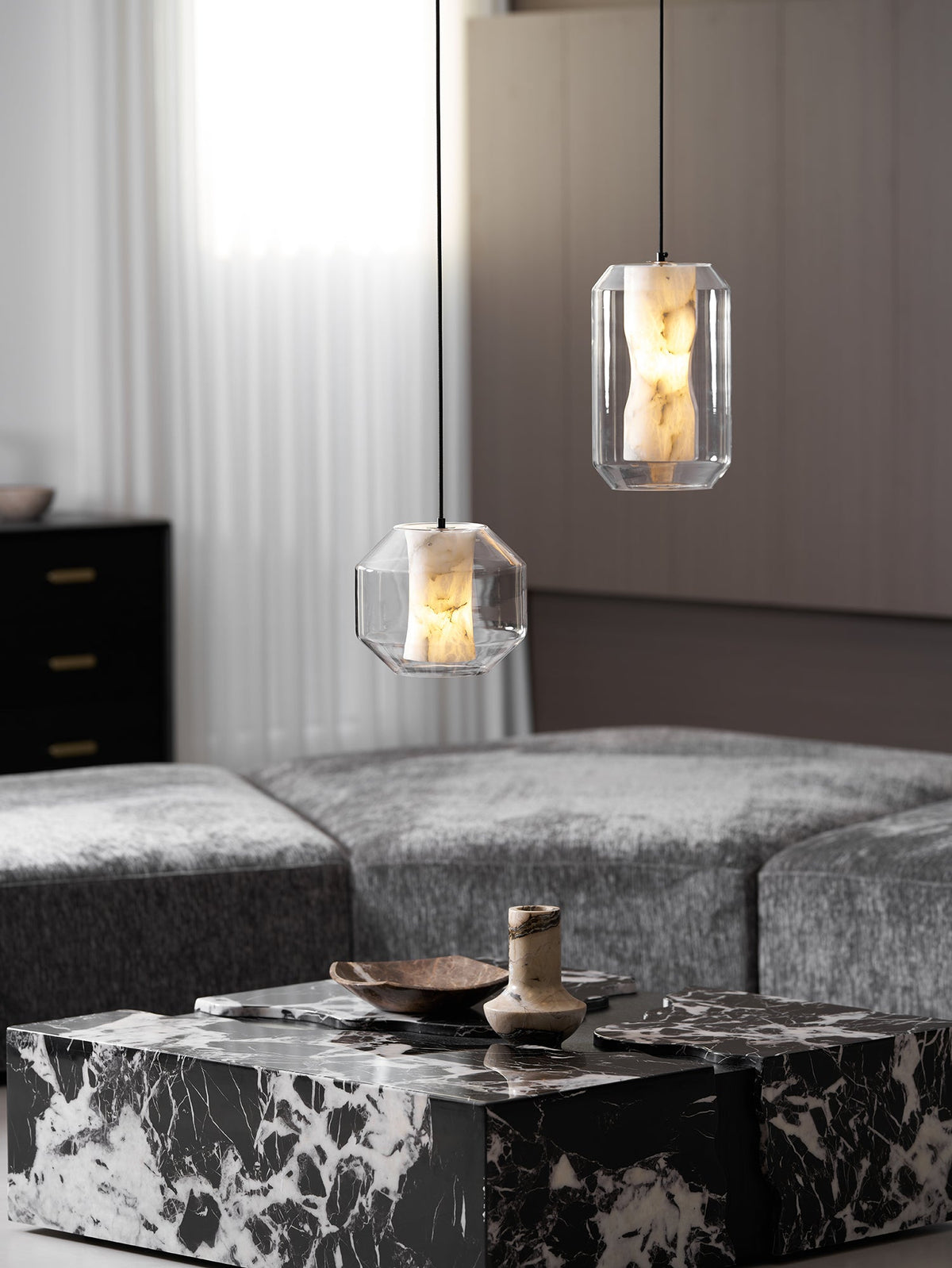 Two Clérachic pendants at different heights above a black and white marble coffee table and grey seating, one wide and one tall.