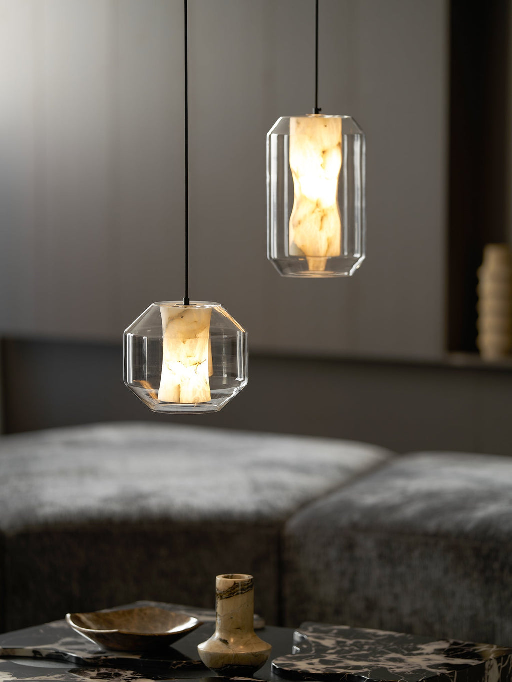 Closer view of a wide and a tall Clérachic pendant above a marble table with a shallow dish and a small vase, against dark wood panelling.
