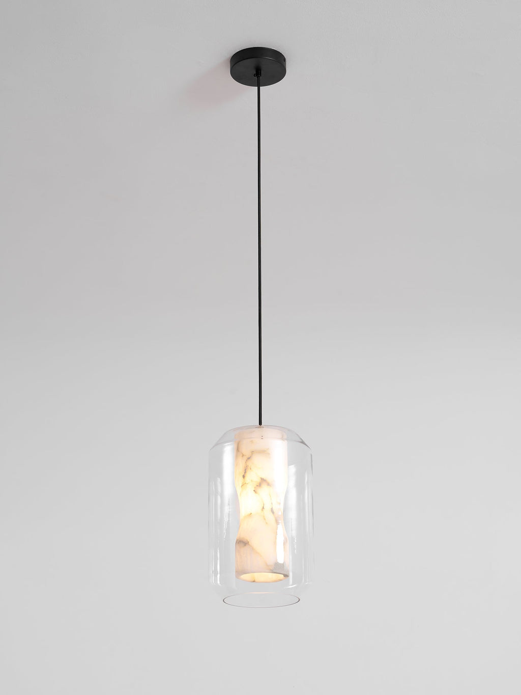 A Clérachic pendant on a single black cord and round black canopy against a pale wall, the alabaster core just visible inside clear glass.