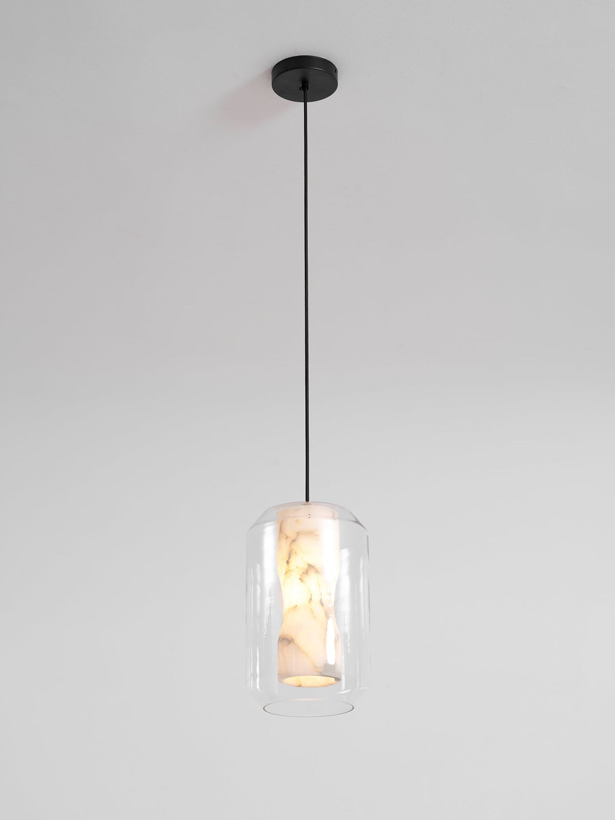 A Clérachic pendant on a single black cord and round black canopy against a pale wall, the alabaster core just visible inside clear glass.
