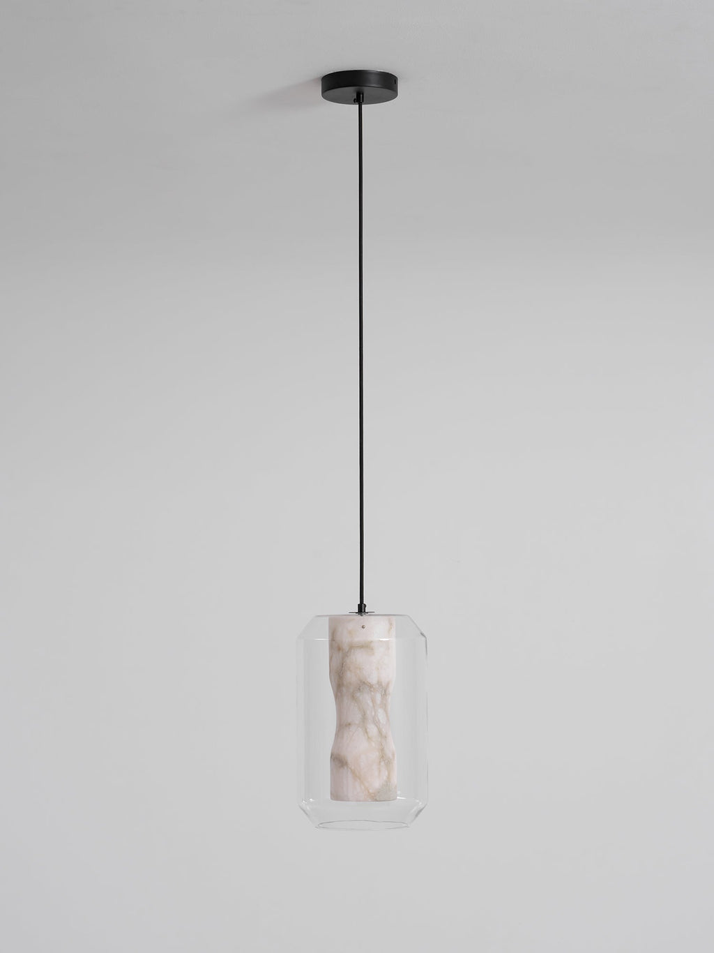 A tall Clérachic pendant unlit on a long black cord and round canopy, its pale veined alabaster seen inside clear glass on a light grey wall.