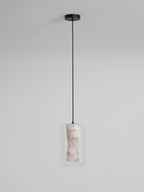 A tall Clérachic pendant unlit on a long black cord and round canopy, its pale veined alabaster seen inside clear glass on a light grey wall.