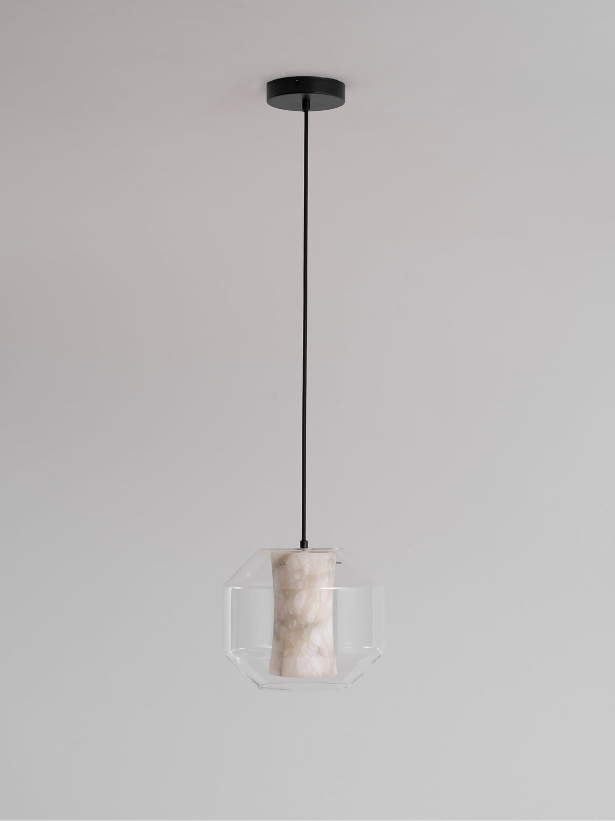 A wide Clérachic pendant hanging from a round black canopy against pale grey, its alabaster column glowing gently inside the glass.