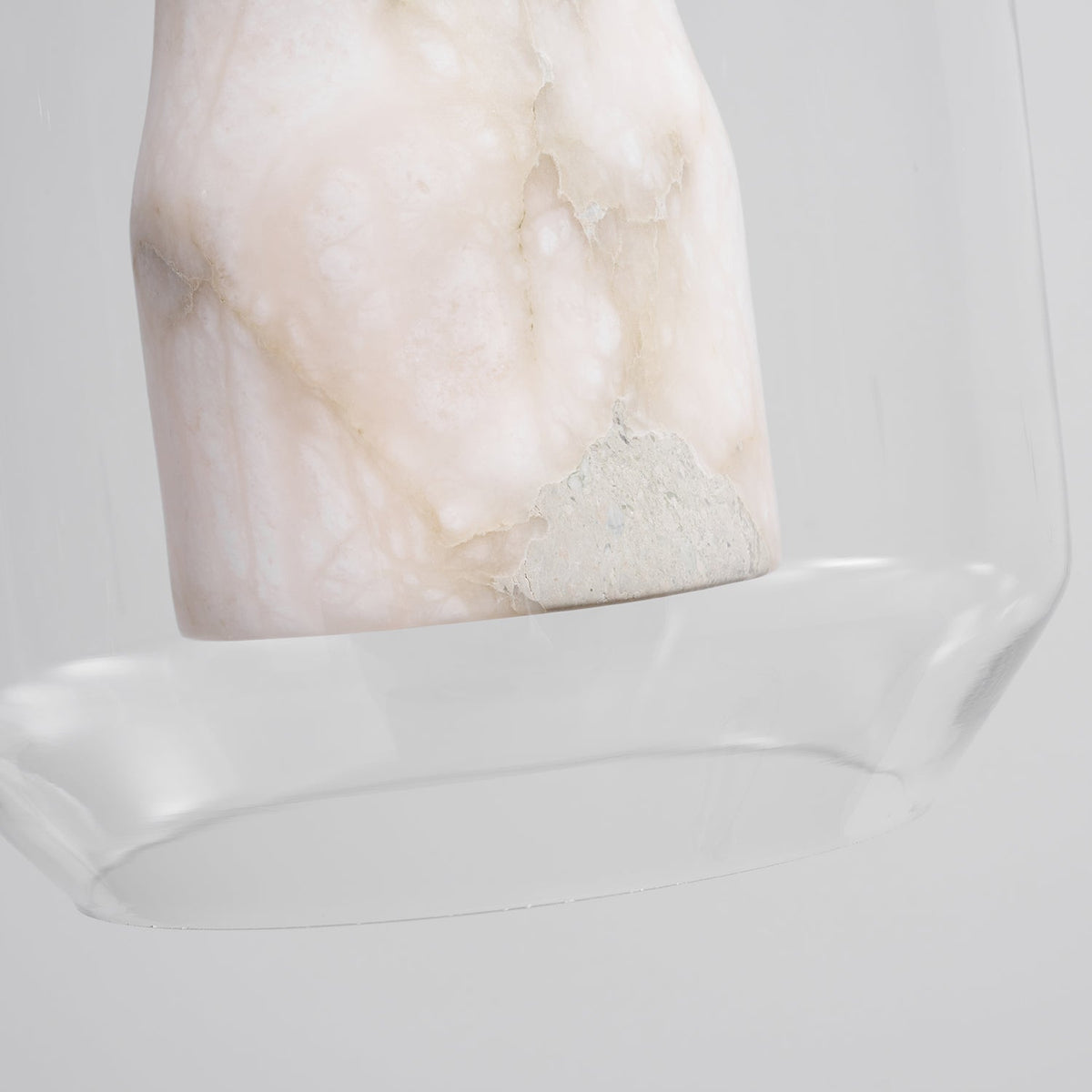 Close view of the unlit base of the alabaster column inside the glass shell of this Clérachic pendant, showing its pale veining and rough stone patch.