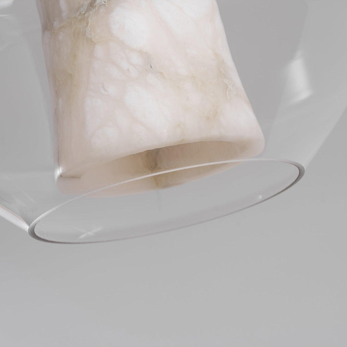 View from below of the alabaster column and the rim of the clear glass shell on this Clérachic pendant, on a pale grey backdrop.
