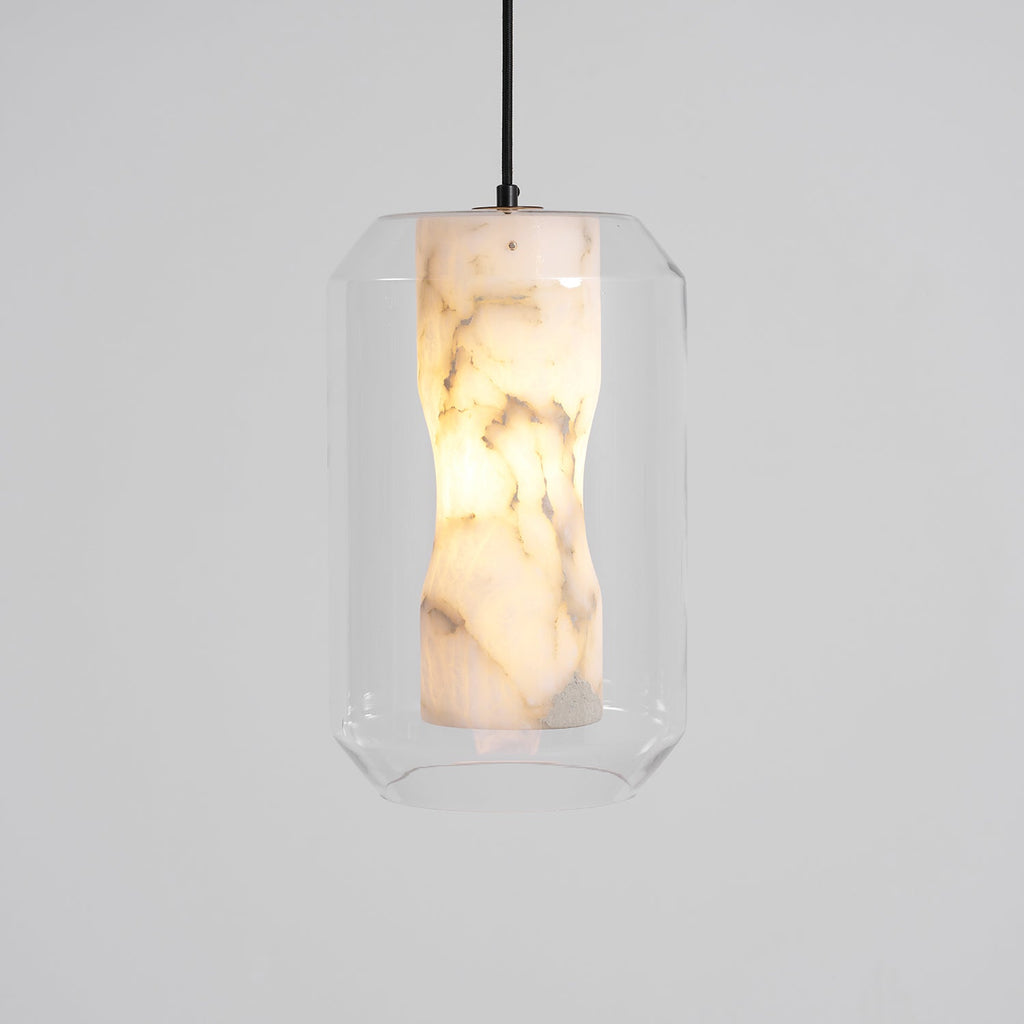 A tall Clérachic pendant on a black cord against pale grey, the waisted alabaster column glowing with brown veining inside clear faceted glass.