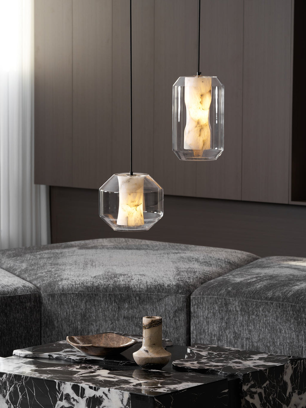 Two Clérachic pendants, one wide and one tall, hang above a marble table and grey seating in front of dark wood panelling.